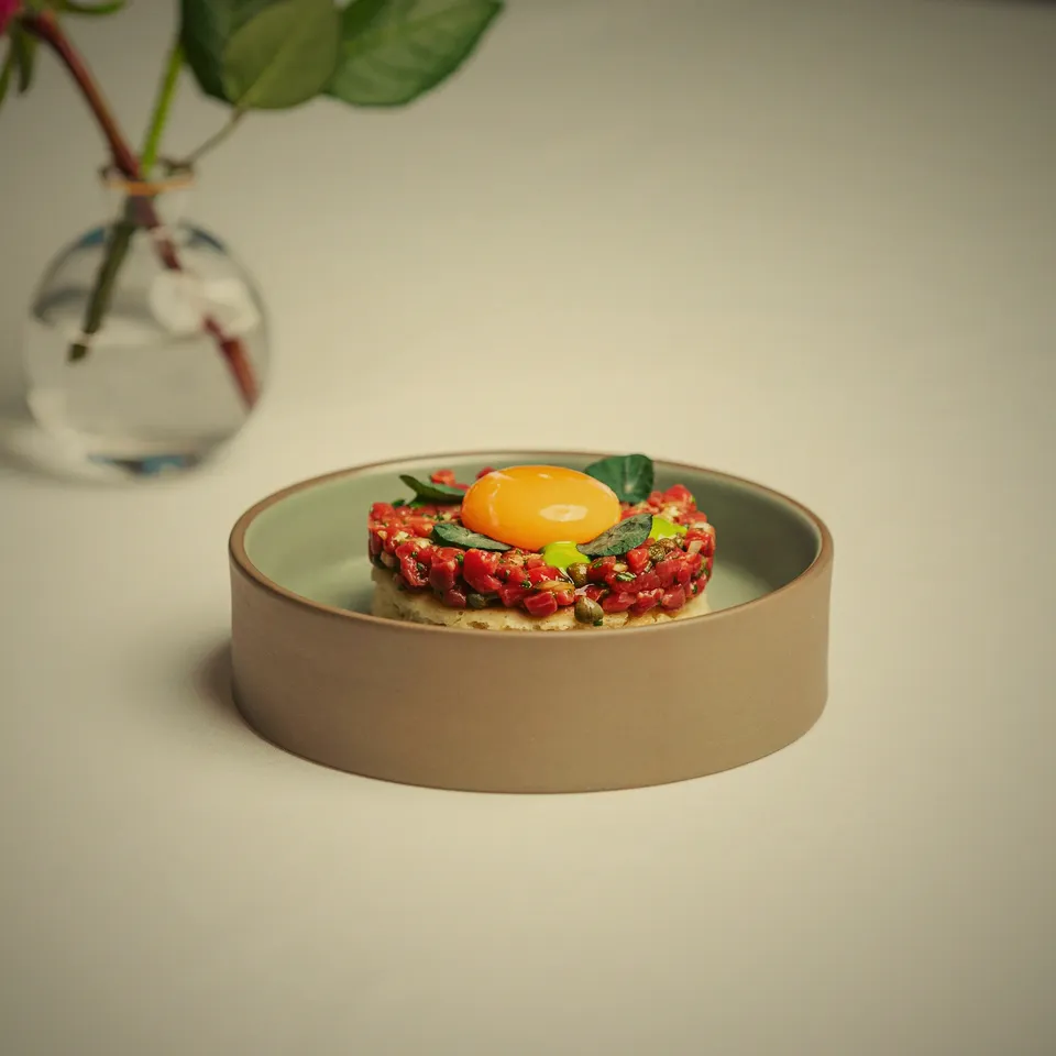 Tartar med äggula och gröna detaljer på ett ljust fat