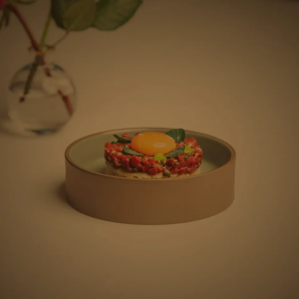 Tartar med äggula och gröna detaljer på ett ljust fat
