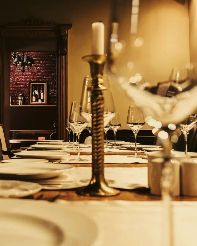 Ljus i mässingsstake och vinglas på ett dukat bord